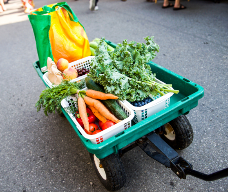 A wagon full of fresh vegetables is being pulled down the street. You cannot see the person pulling it.